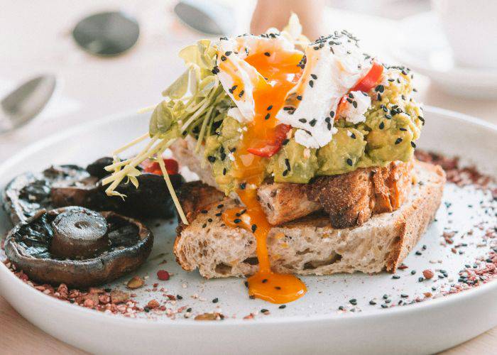 A poached egg and avocado on toast with a side of mushrooms.